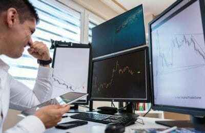 Frustrated cryptocurrency trader staring at computer screens showing Bitcoin price charts stuck at resistance level