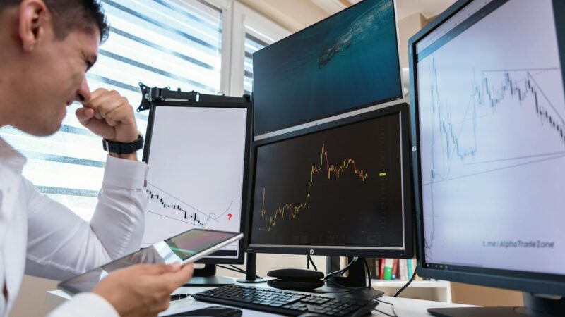 Frustrated cryptocurrency trader staring at computer screens showing Bitcoin price charts stuck at resistance level