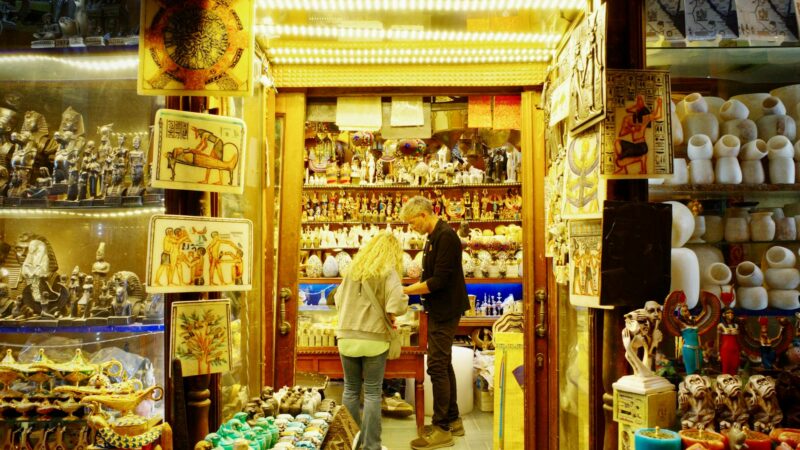 Egyptian customers examining gold jewelry at a busy Cairo gold market shop with display cases of 21-karat pieces