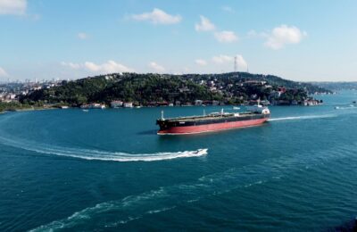Aerial view of large oil tankers passing through a narrow ocean strait with blue water and coastlines visible on both sides
