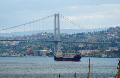 Cargo ships and oil tankers navigating through a narrow ocean strait passage representing Hormuz reopening and its impact on oil prices