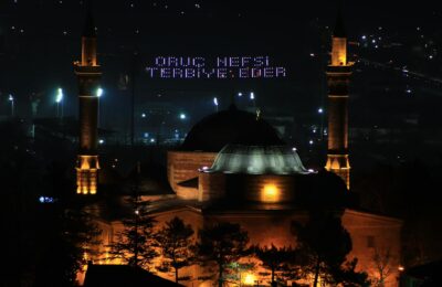 Traditional Ramadan lantern (fanous) illuminated at sunset near a mosque during the holy month
