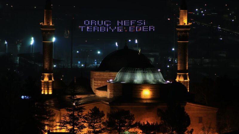 Traditional Ramadan lantern (fanous) illuminated at sunset near a mosque during the holy month