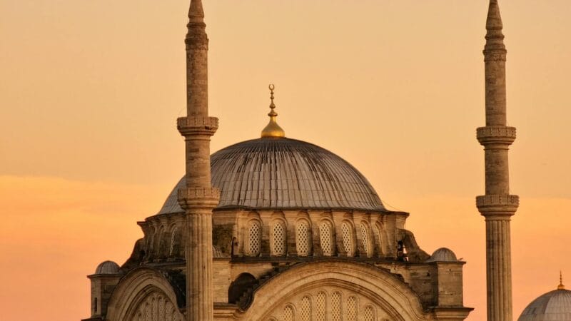 Tourists visiting a historic mosque in Istanbul Turkey at sunset with the city skyline in the background