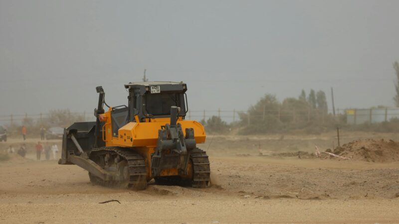 Large construction site in the desert with heavy machinery and equipment surrounded by sand dunes showing a mega-project under development