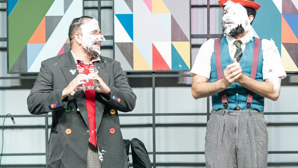 An Arabic comedy stage performance with an audience laughing in a warm-lit theater