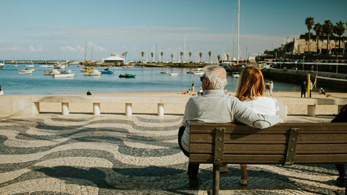Relaxed elderly expat couple walking along a Mediterranean beach at sunset