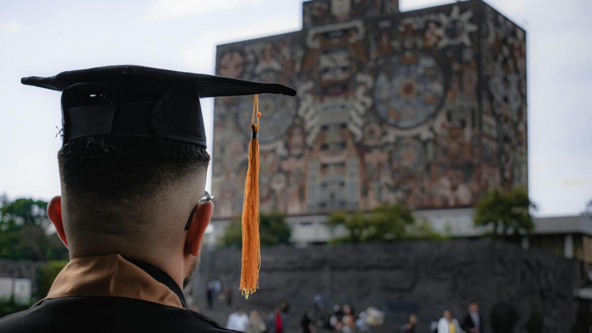 Students walking through a modern Middle Eastern university campus with palm-lined plaza, contemporary library building, and graduates in regalia