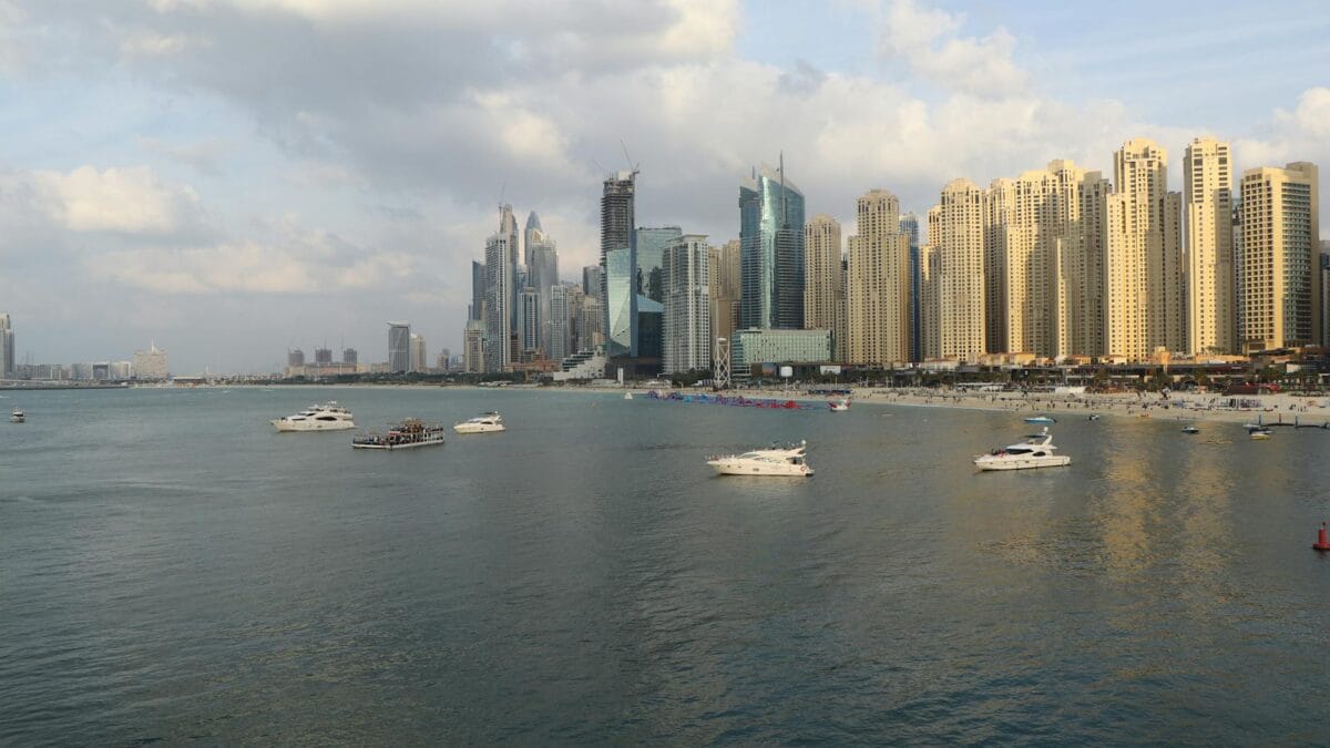 Dubai Marina waterfront at sunset with modern apartment towers, palm-lined promenade, and yachts moored along the harbour