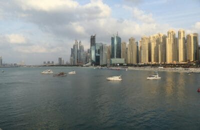 Dubai Marina waterfront at sunset with modern apartment towers, palm-lined promenade, and yachts moored along the harbour