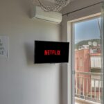 A large television screen displaying the Netflix red logo in a home entertainment setup with ambient lighting