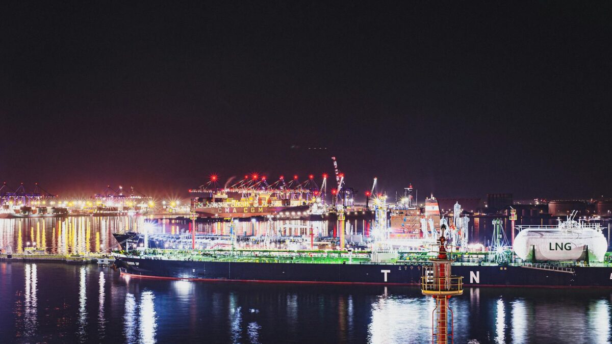 Illuminated LNG facility at Qatar port with shipping containers and tankers at night