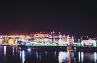 Illuminated LNG facility at Qatar port with shipping containers and tankers at night